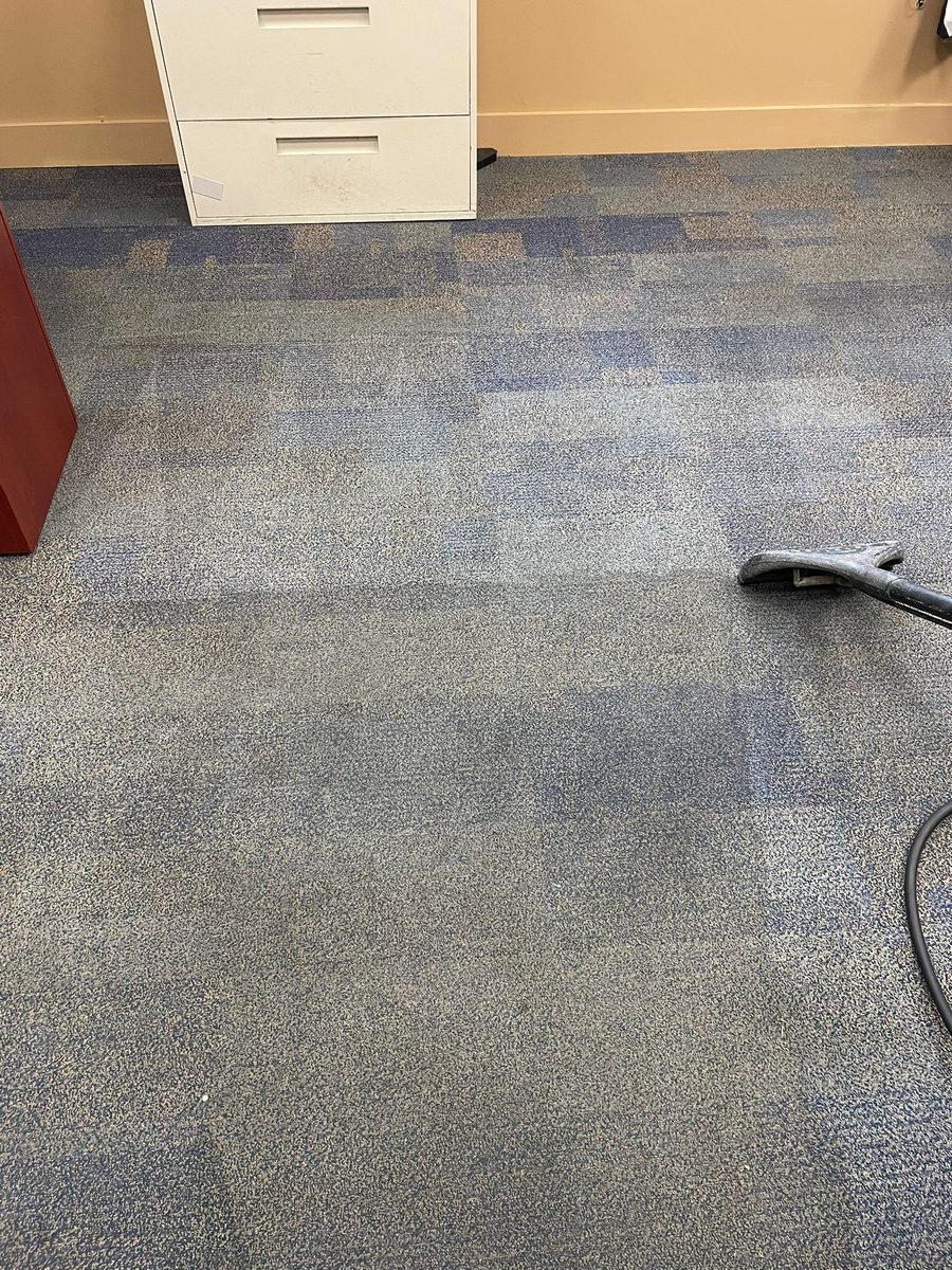 Blue speckled office carpet tiles with the cleaned section visibly brighter than the uncleaned section and the wand resting on the floor