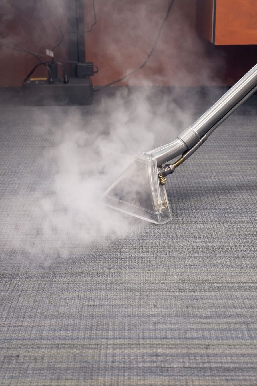Steam rising from a carpet cleaning wand as it passes over grey commercial carpet