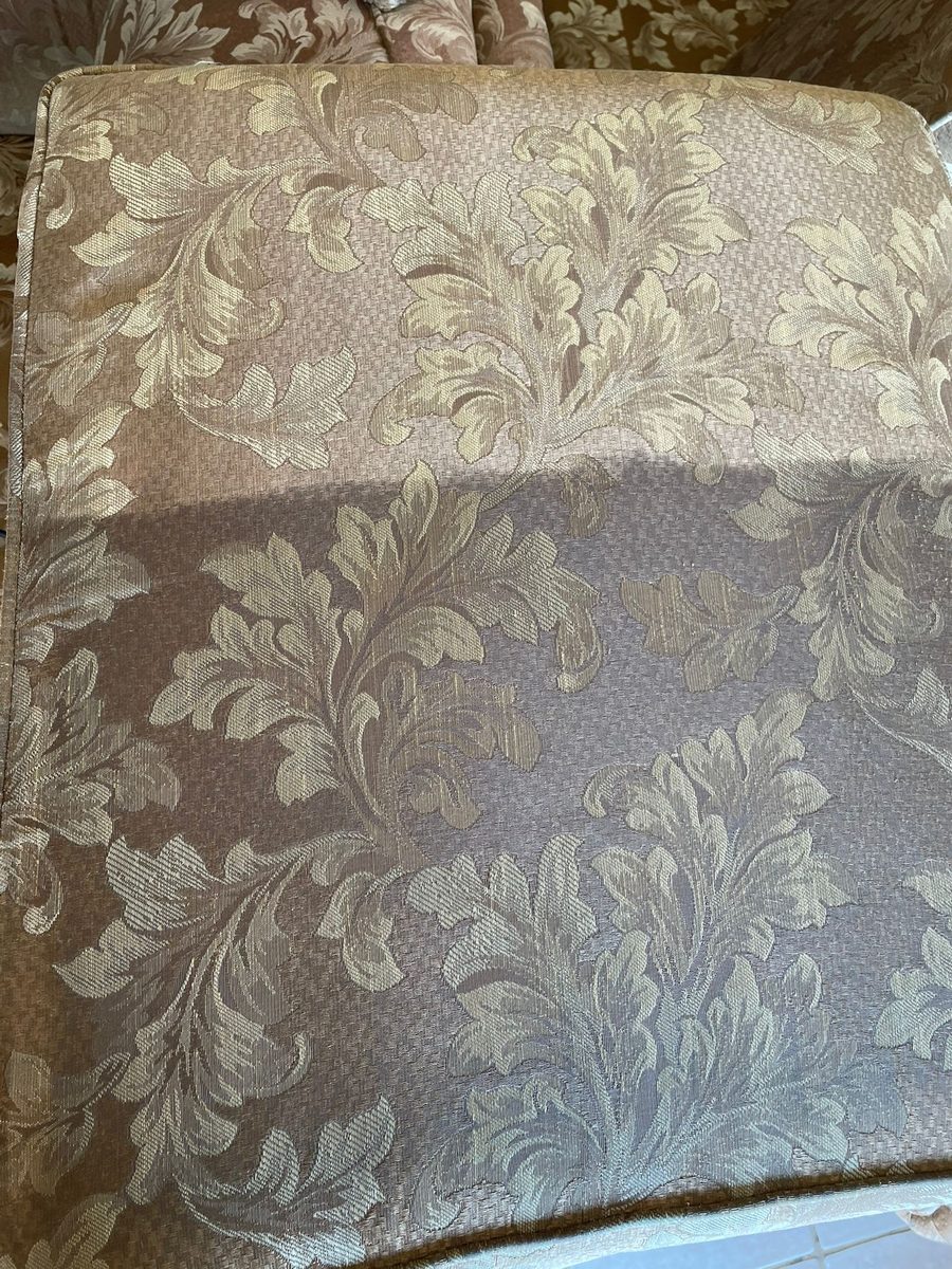 Damask upholstered chair seat with the top half cleaned to a light gold and the bottom half still dull brown